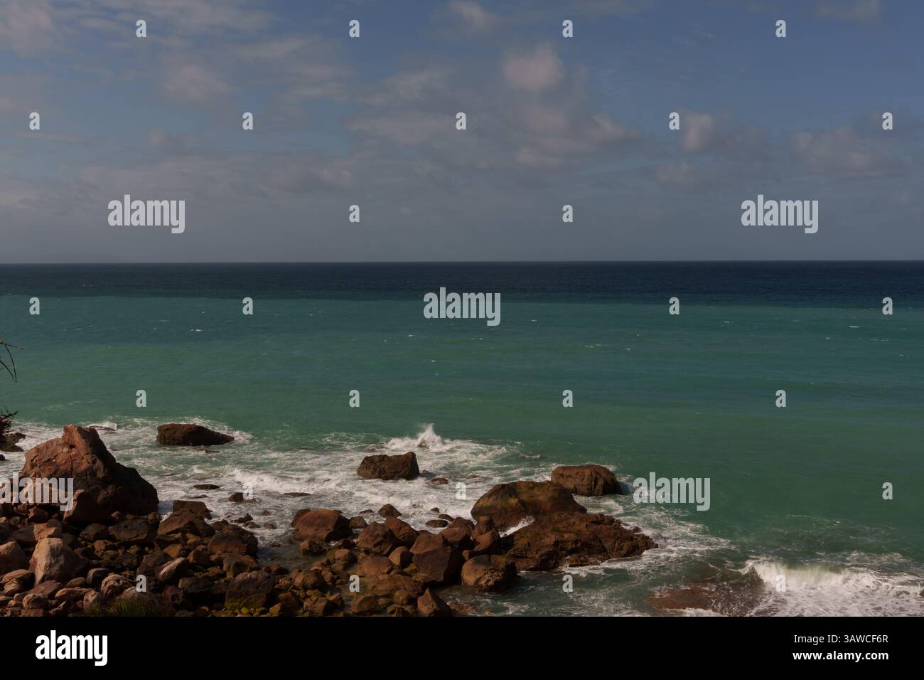 Vagues turquoises se brisant contre le rivage rocheux sous ciel nuageux Banque D'Images