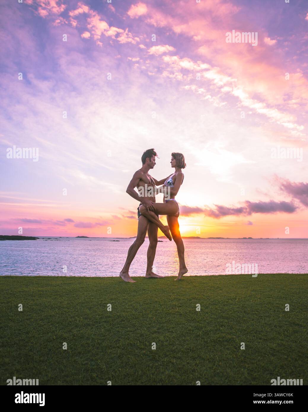 Couple sportif silhouettes homme et femme faisant danseur romantique pose sur l'herbe devant un beau coucher de soleil sur la mer. Voyage ensemble, relation. Banque D'Images Couple sportif silhouettes homme et femme faisant danseur romantique pose sur l'herbe devant un beau coucher de soleil sur la mer. Voyage ensemble, relation. Banque D'Images