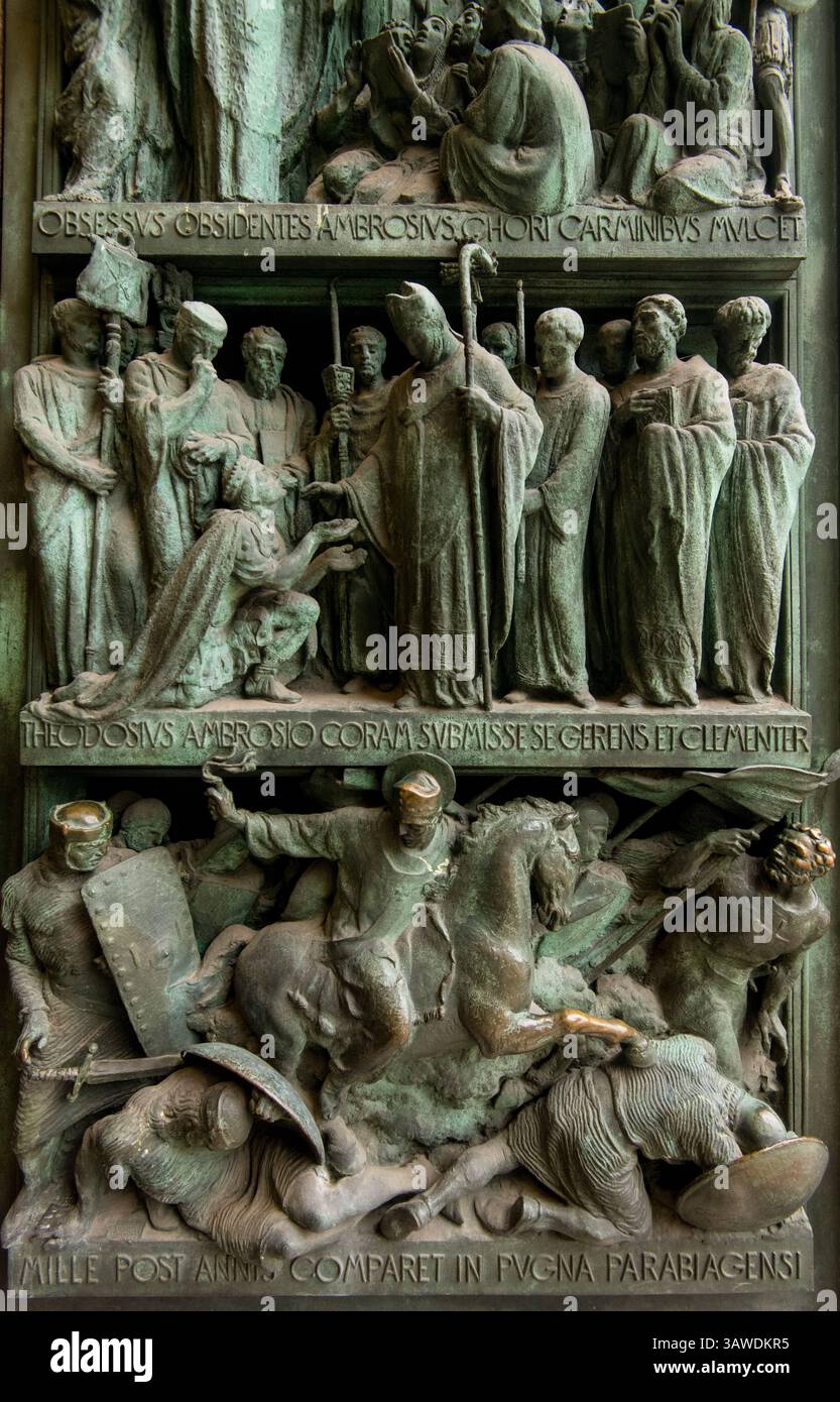 Détail du panneau de bronze de la porte d'entrée gauche au Duomo di Milano représentant des scènes avec des figures en relief et des inscriptions latines. « OBSESSIS OBSIDENTES AMBROSIVS. CHORI CARMINBYS MVLCET ;' 'THEODOSIVS AMBROSIO CORAM SVBMISSE SE GERUNS ET CLEMENTER' ET 'MILLE POST ANNIS COMPARET IN PVGNA PARABIAGENSI.' Cette scène représente probablement un événement historique ou religieux impliquant un membre Ambrose, une figure importante de l'histoire de Milan. Les portes en bronze de la cathédrale de Milan sont connues pour leurs détails complexes et leurs représentations d'événements historiques et religieux. Milan, Italie. Banque D'Images