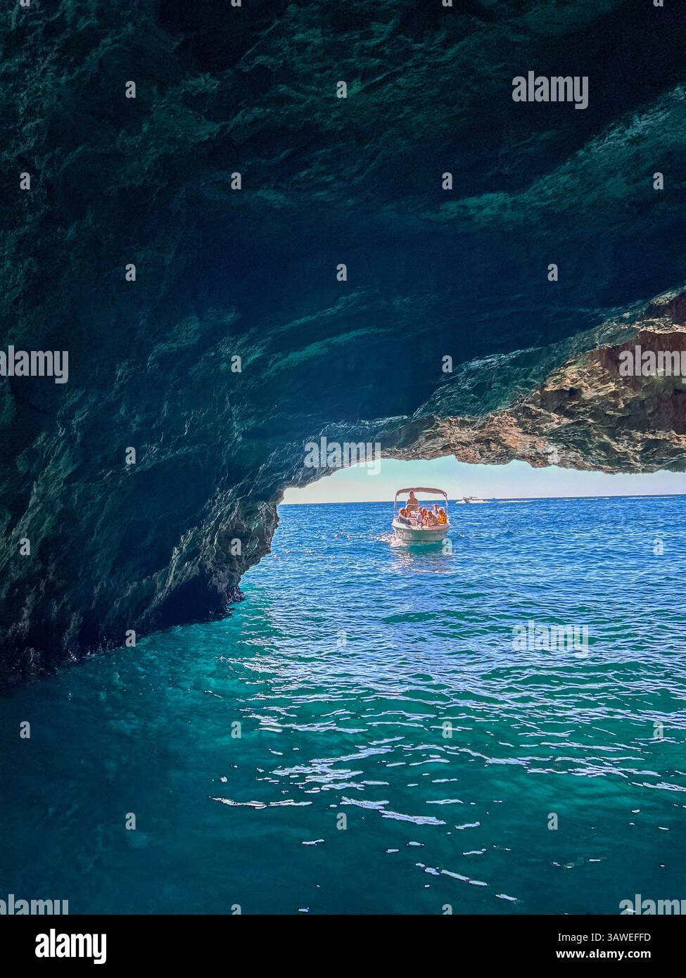 Un petit bateau pénètre dans la fascinante grotte bleue au Monténégro, rayonnant de reflets bleus vifs. - Image de stock capturée avec un smartphone