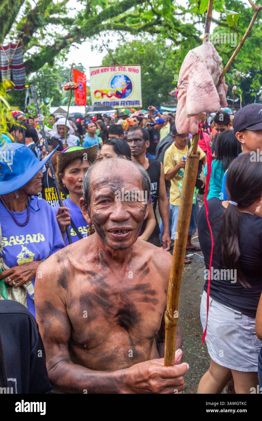 Un homme philippin dans un esprit festif tient un bâton avec de la viande pendant le Festival ATI-ATI à Aklan, Philippines, mettant en évidence une tradition culturelle unique Banque D'Images