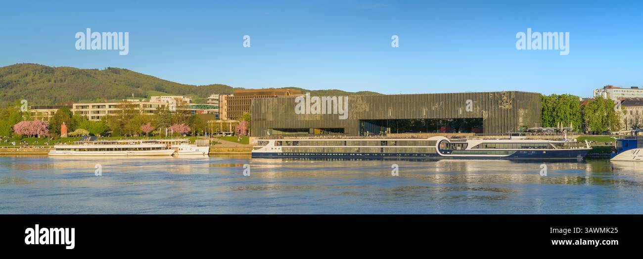 Spring in Linz met en valeur la scène vibrante le long du Danube, où les arbres en fleurs encadrent un musée moderne. Les visiteurs profitent de moments de détente sur boa Banque D'Images