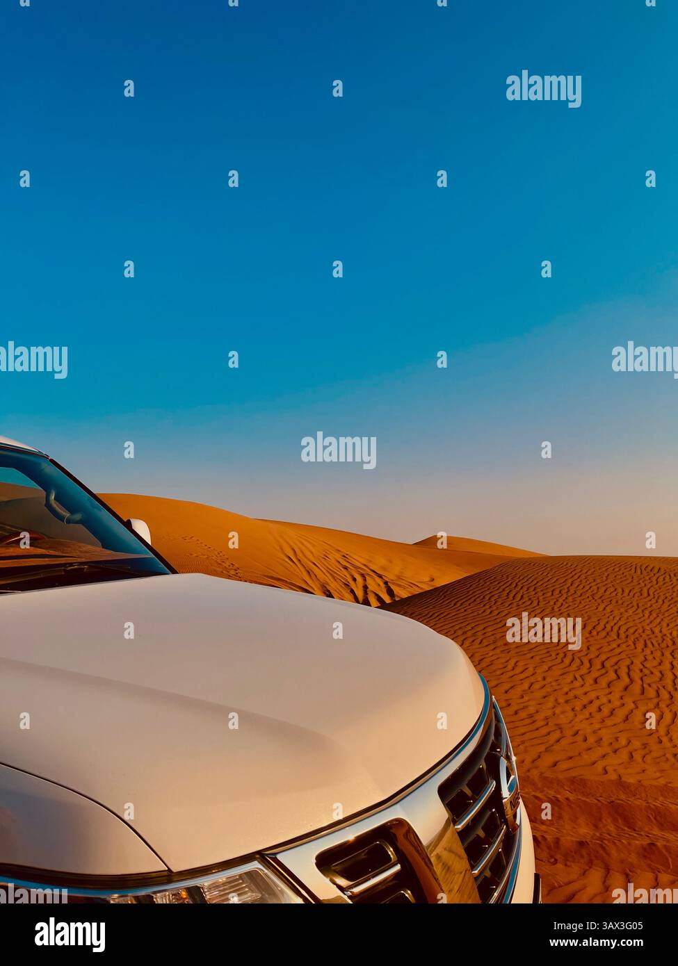 'SUV garé dans le désert arabe près des dunes de sable sous un ciel bleu clair aux Émirats arabes Unis, représentant le voyage de luxe, l'aventure et le voyage' - Image de stock capturée avec un smartphone