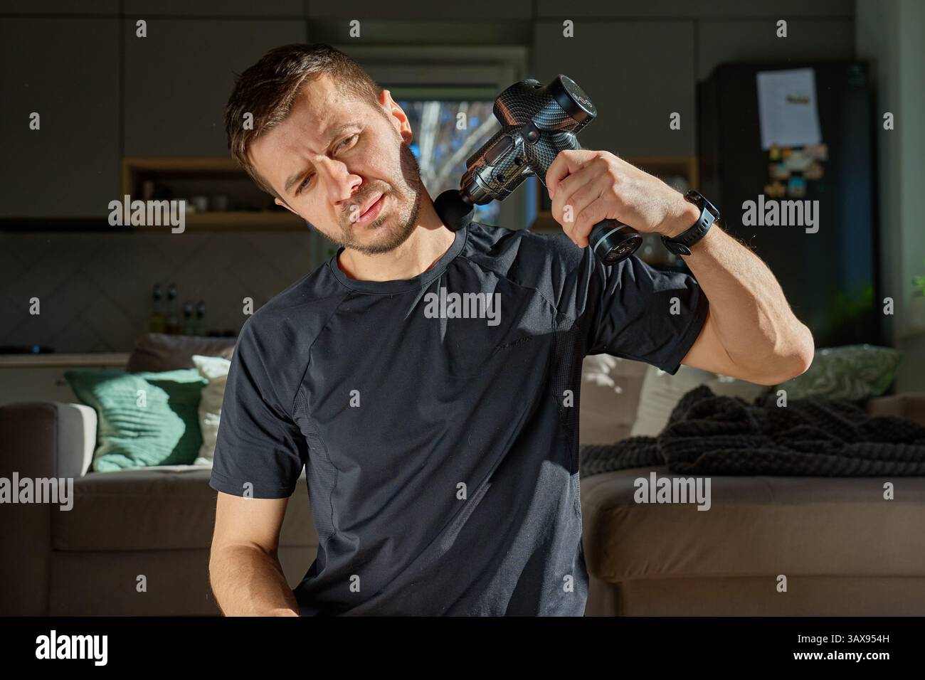 L'homme applique un pistolet de massage pour soulager la tension dans la région du cou et des épaules. Athlète masculin pratiquant une thérapie d'auto-massage avec un dispositif de percussion pour la récupération ultérieure Banque D'Images