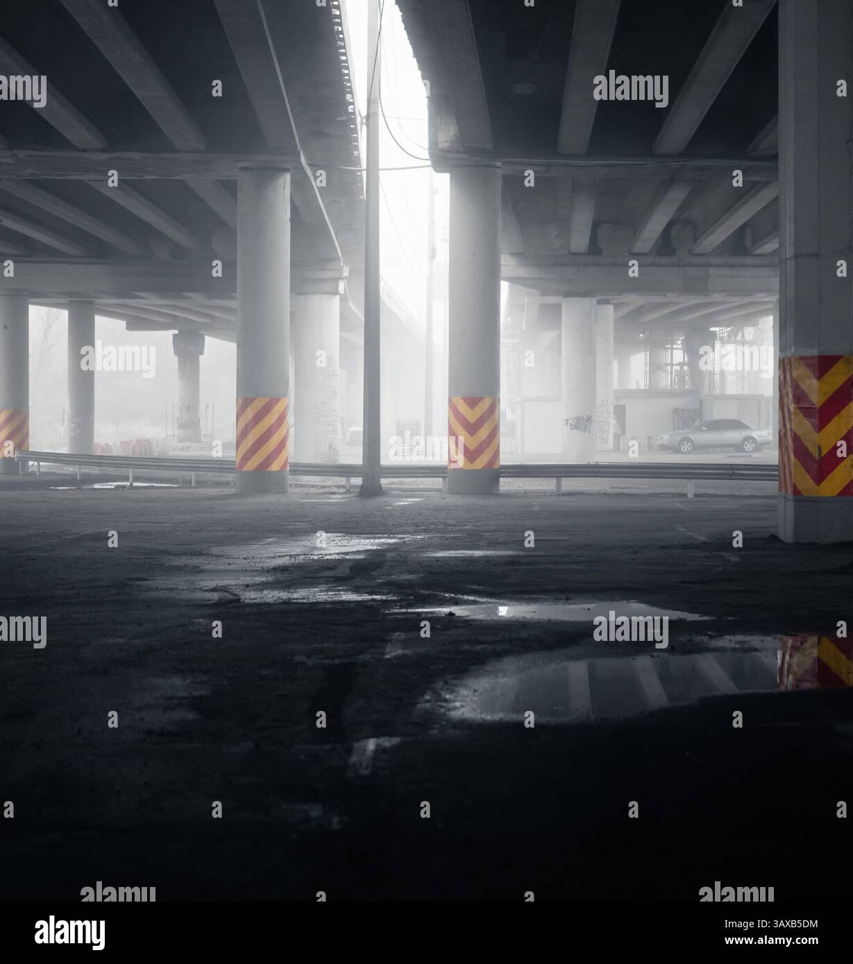 Vue en perspective de deux ponts en béton recouverts d'un épais brouillard. Flaques d'eau sur un parking asphalté sous le pont, faible visibilité le matin de novembre. Banque D'Images