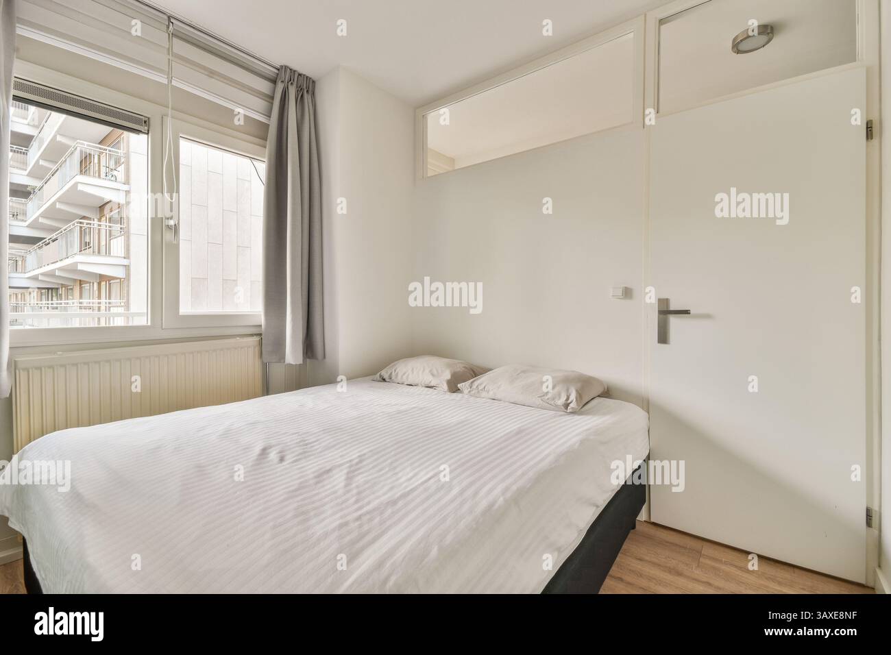 Une chambre lumineuse et aérée avec un décor minimaliste, de grandes fenêtres et un lit confortable, mettant l'accent sur la simplicité et la fonctionnalité. Banque D'Images