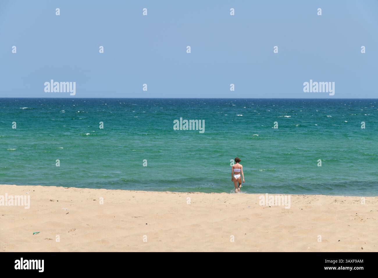 Jeune fille en bikini blanc se relaxant sur le sable blanc de Jebel Sifah public Beach. Sultanat d'Oman. Banque D'Images