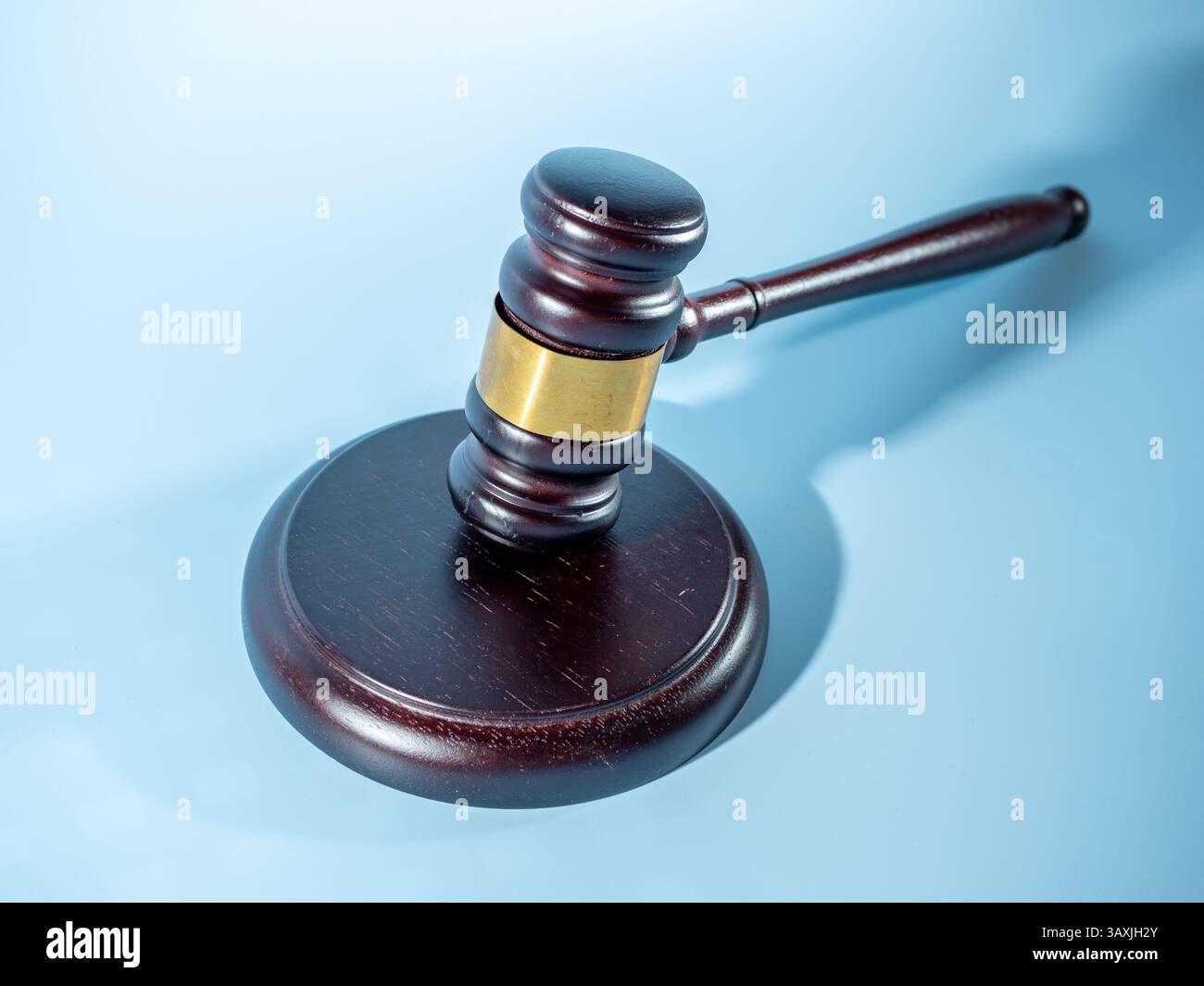 Un marteau en bois avec une bande d'or, reposant sur une base circulaire sur un fond bleu clair Banque D'Images