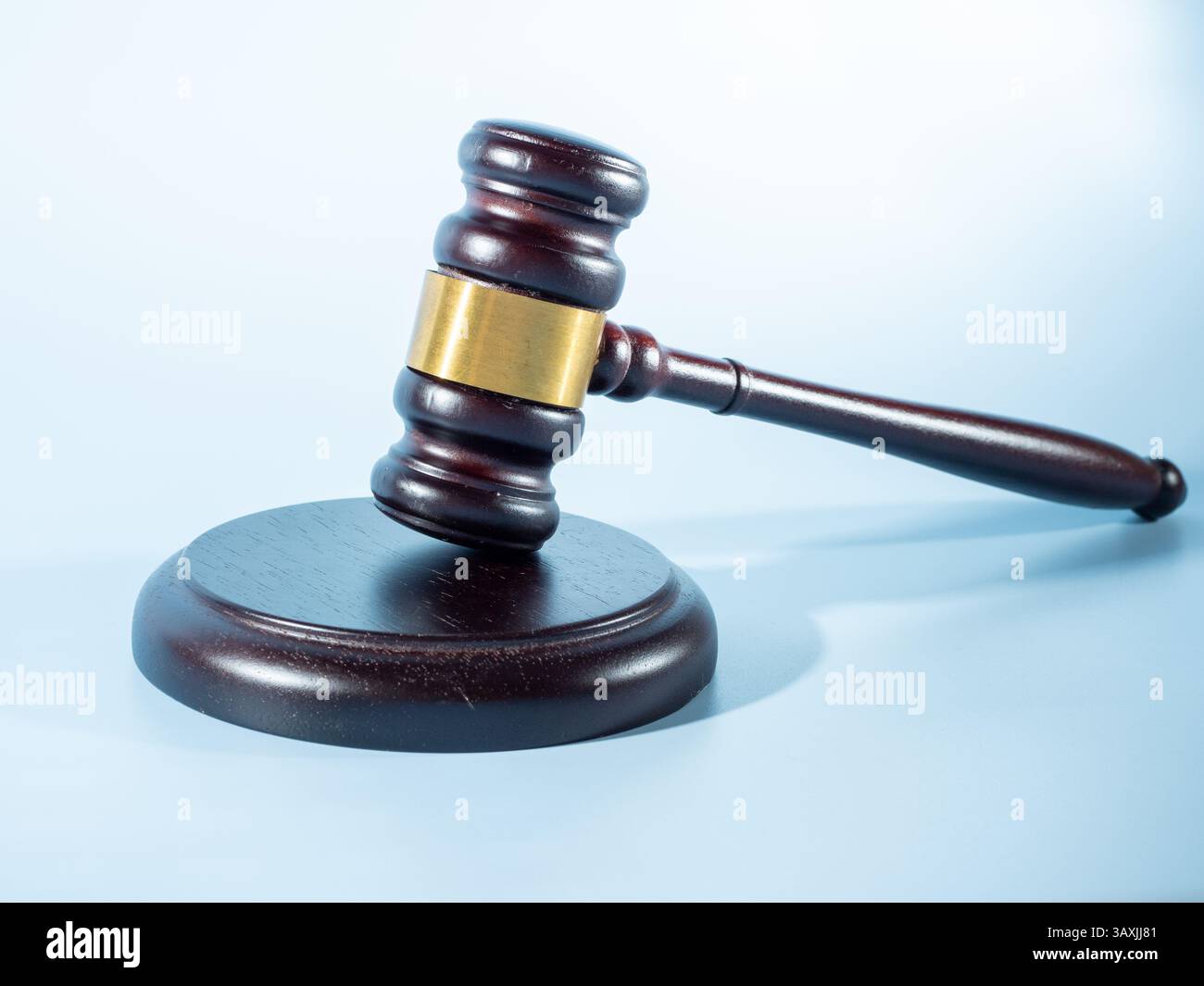 Un marteau en bois avec une bande d'or, reposant sur une base circulaire sur un fond bleu clair Banque D'Images