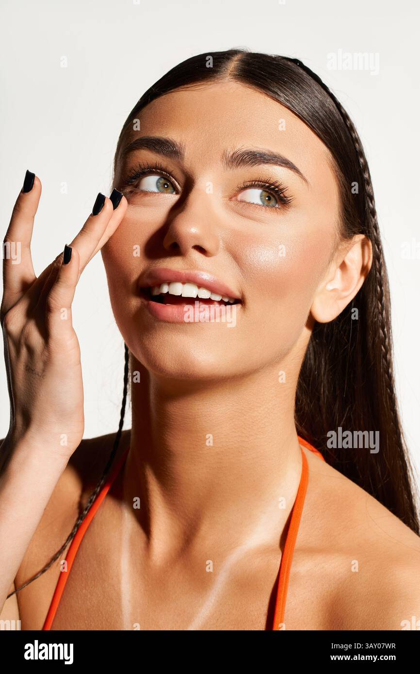 Une jeune femme sourit en appliquant de la crème solaire, mettant en valeur sa peau éclatante embrassée par le soleil. Banque D'Images