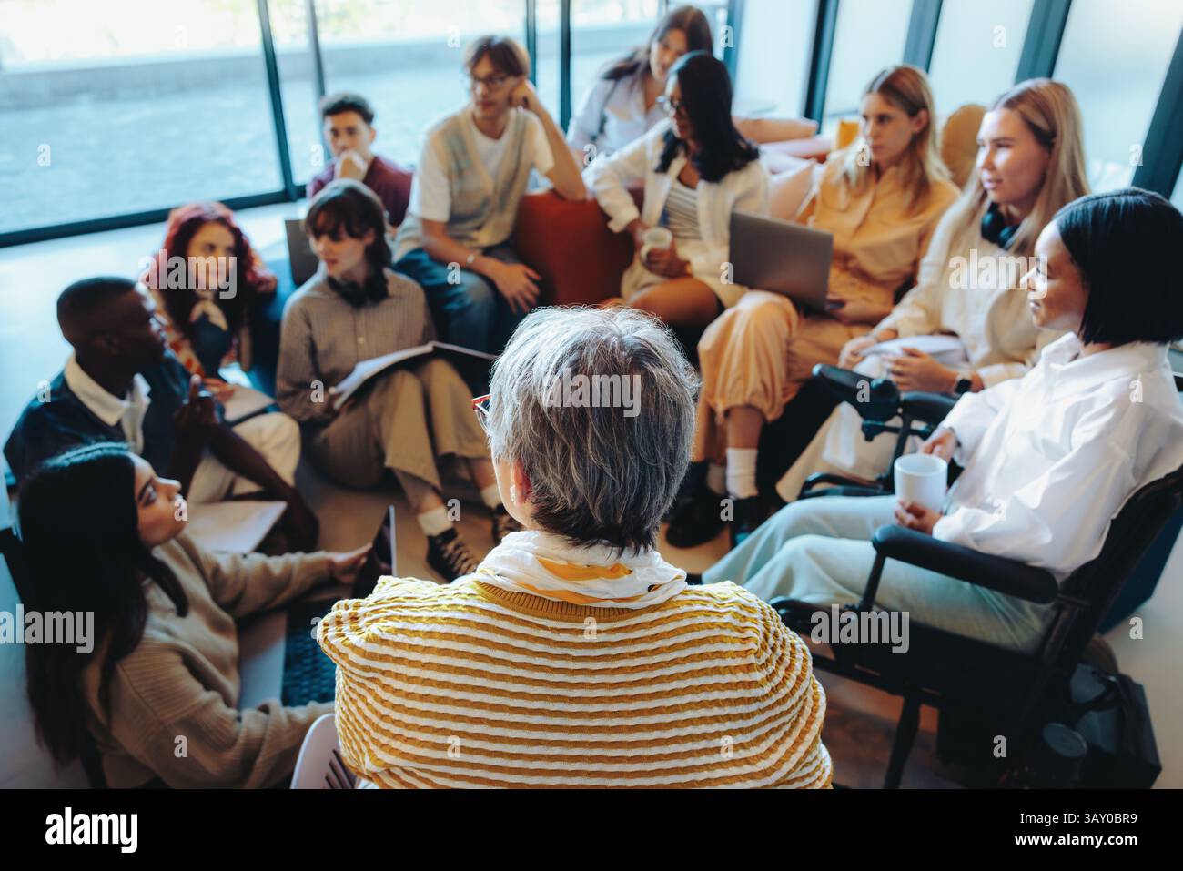 Un groupe d'élèves divers participent à une discussion informelle en classe dirigée par un enseignant, favorisant l'apprentissage interactif et l'éducation inclusive. Banque D'Images