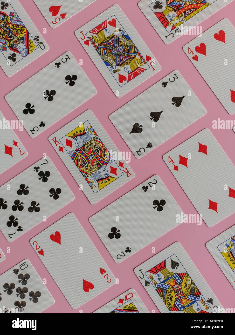 cartes à jouer disposées sur un fond rose. Les cartes sont disposées dans un motif répétitif, avec un mélange de différentes combinaisons et valeurs. - Image de stock capturée avec un smartphone