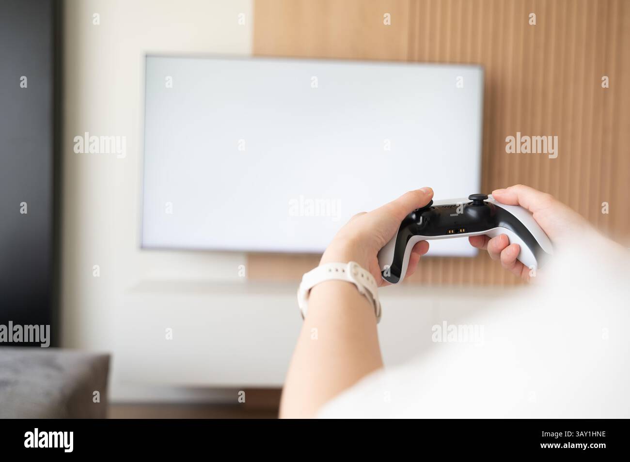 Un gamer dédié se prélasse confortablement sur un canapé confortable, saisissant une manette et regardant un écran de télévision vierge Banque D'Images