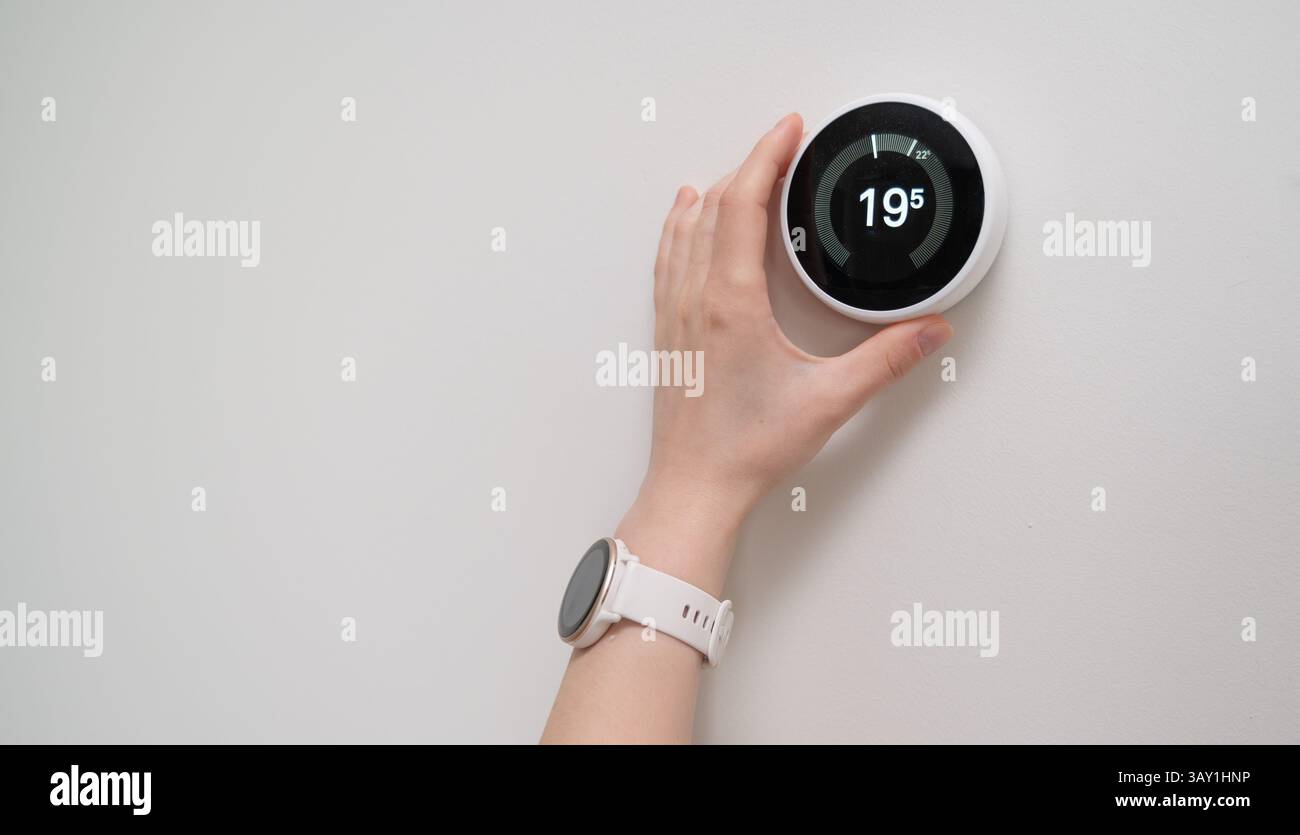 Une main ajustant un thermostat intelligent affichant 19C pour l'efficacité énergétique Banque D'Images