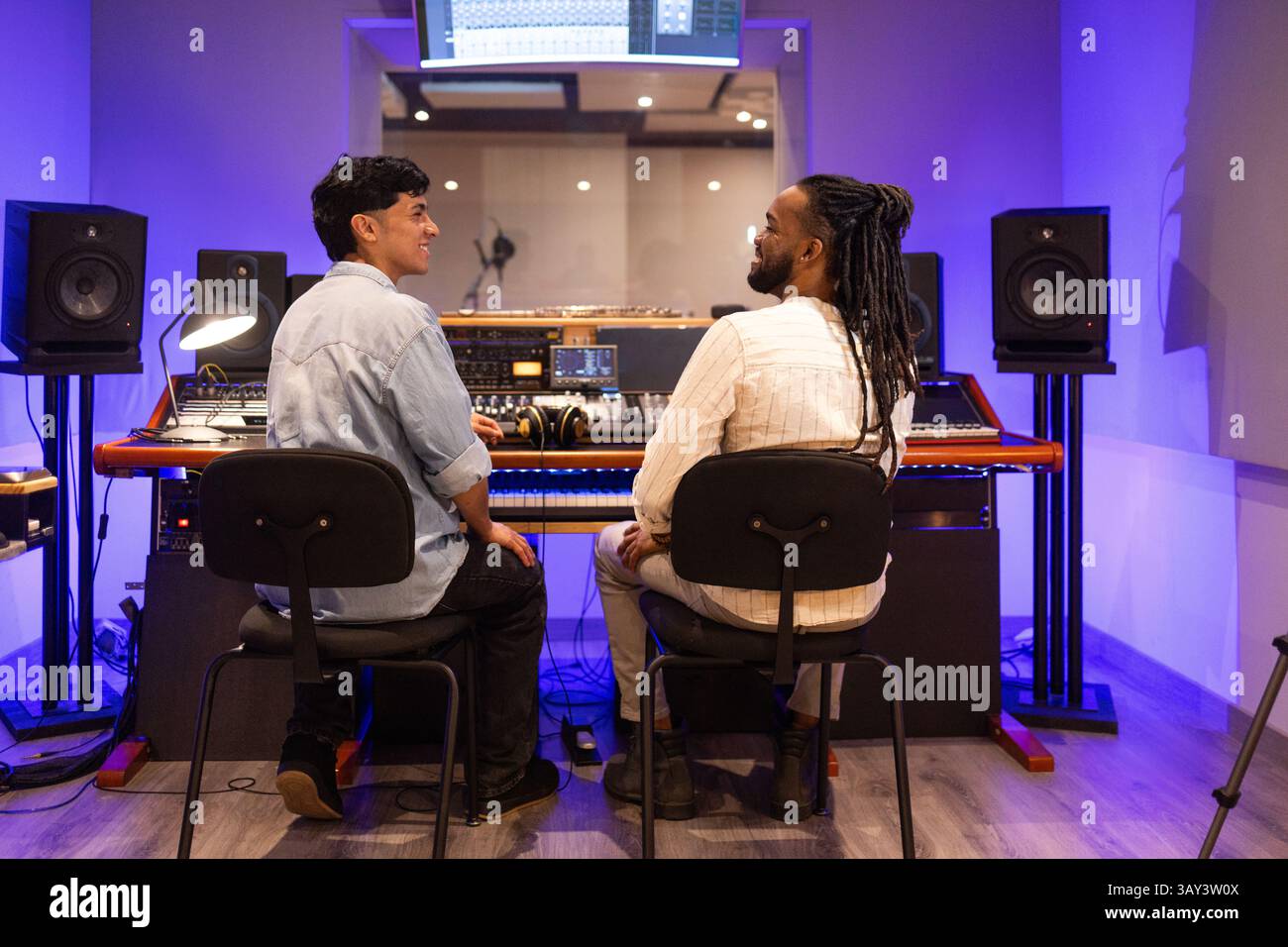 Deux hommes collaborant dans un studio d'enregistrement professionnel, entourés d'équipements audio et d'un éclairage bleu ambiant. Parfait pour représenter un mu créatif Banque D'Images