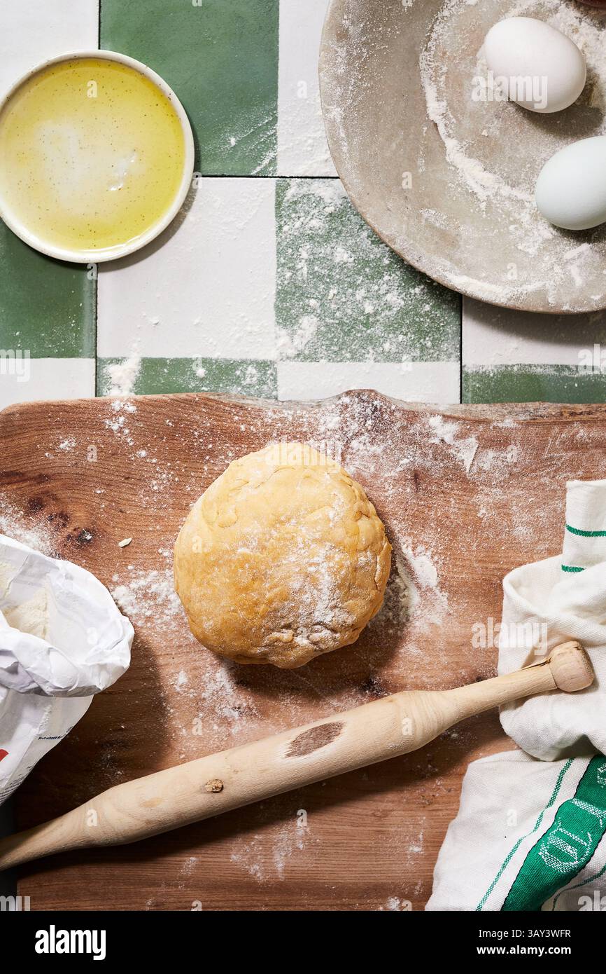 Vue de dessus d'une cuisine rustique pour la fabrication de pâtes et pâtisseries maison, avec une boule de pâte bien pétrie sur une planche de bois farinée, un rouleau à pâtisserie, Banque D'Images