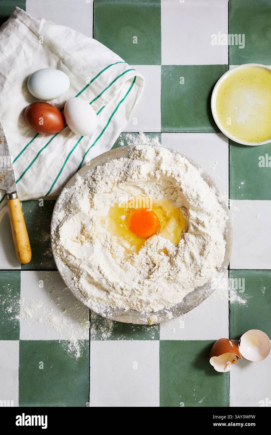 Vue de dessus d'une préparation de pâtisserie maison avec des œufs, de la farine et un bol de mélange fouetté sur une surface carrelée verte et blanche. Un cadre rustique pour hom Banque D'Images