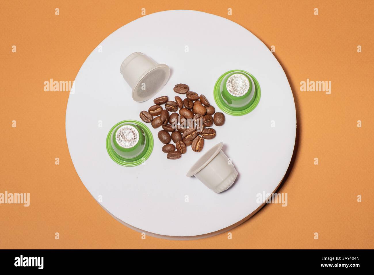 Capsules de café biodégradables et grains dispersés disposés sur une surface circulaire sur un fond orange. L'image met en évidence le contraste et l'har Banque D'Images