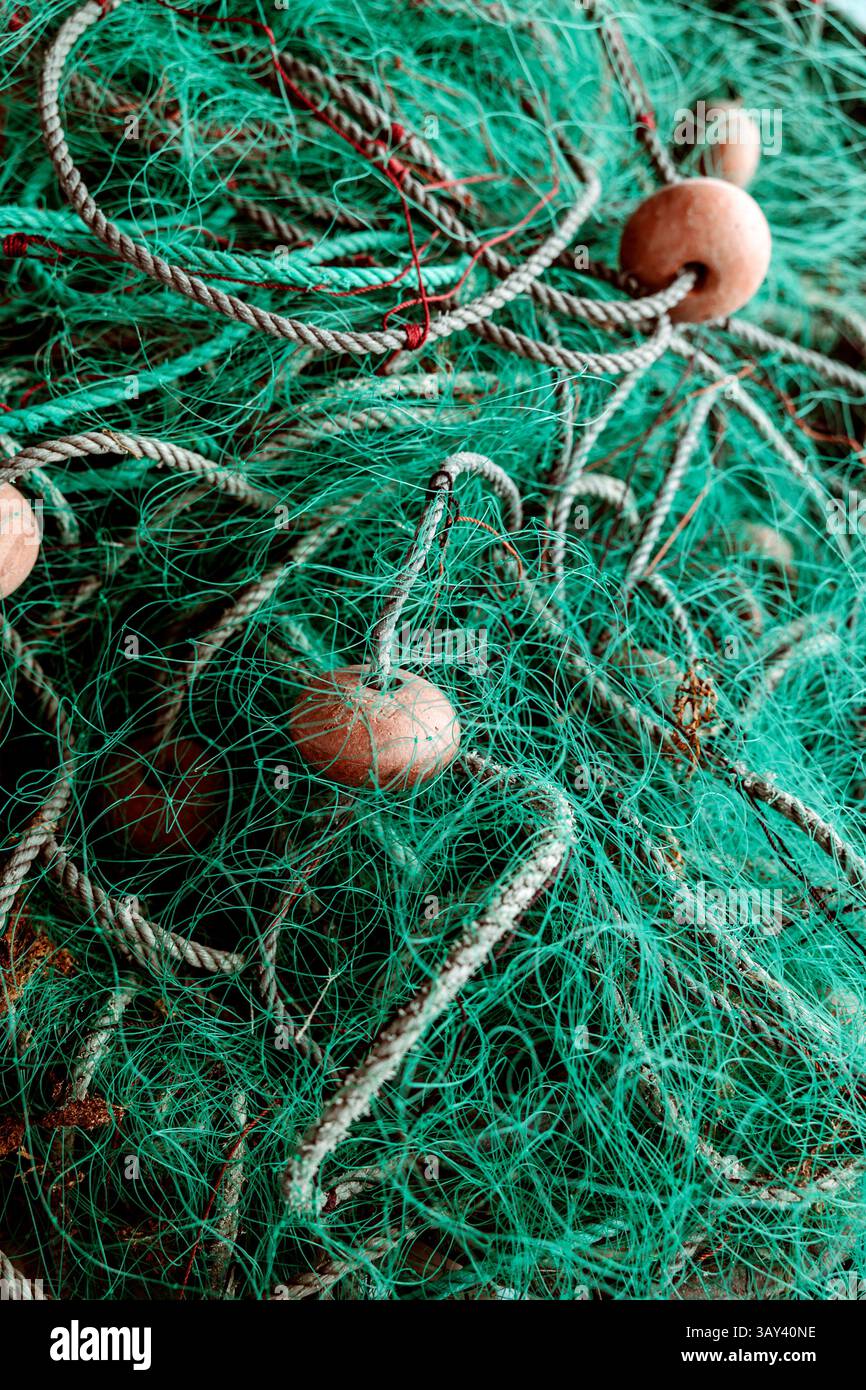 Gros plan d'un filet de pêche affichant des textures et des motifs complexes. Le filet a de la ficelle verte et est enchevêtré avec des cordes. Les bouées en bois ajoutent du contraste et Banque D'Images