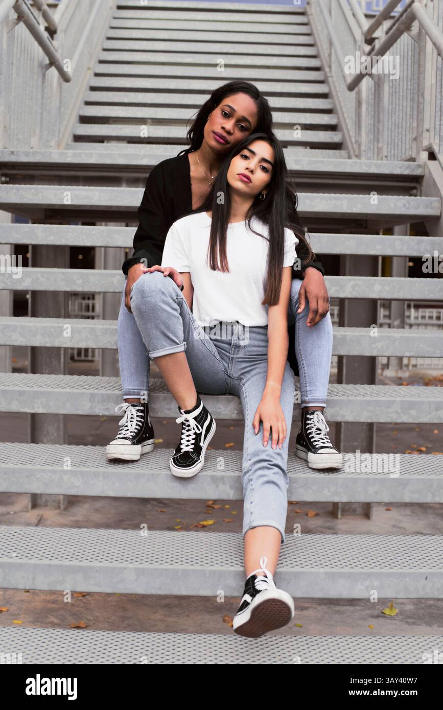 Deux amis élégants se détendent sur les escaliers urbains, mettant en valeur la mode décontractée. Jeans, t-shirts et baskets mettent en valeur une ambiance décontractée dans un décor urbain extérieur Banque D'Images Deux amis élégants se détendent sur les escaliers urbains, mettant en valeur la mode décontractée. Jeans, t-shirts et baskets mettent en valeur une ambiance décontractée dans un décor urbain extérieur Banque D'Images
