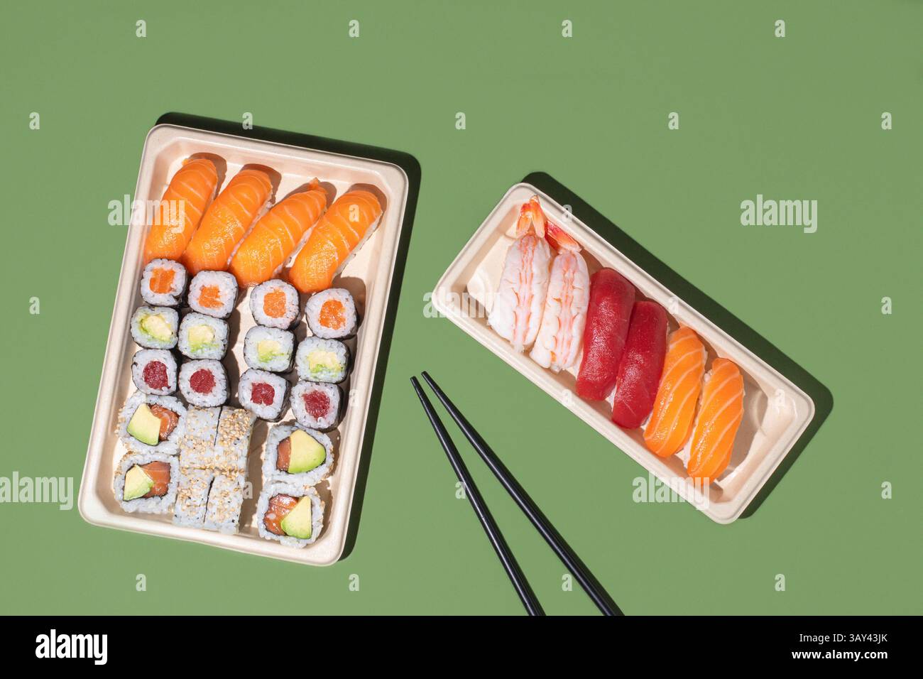 Plan minimaliste au plafond de boîtes à emporter à sushis sur fond vert, avec des rouleaux de nigiri et de maki avec un éclairage directionnel puissant Banque D'Images