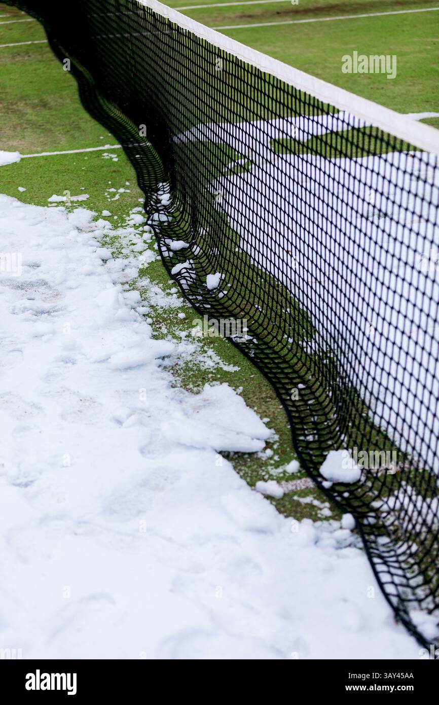 Un court de tennis est partiellement recouvert de neige, créant un contraste saisissant entre la neige blanche et l'herbe verte. Le filet divise la scène, ajoutant un Banque D'Images