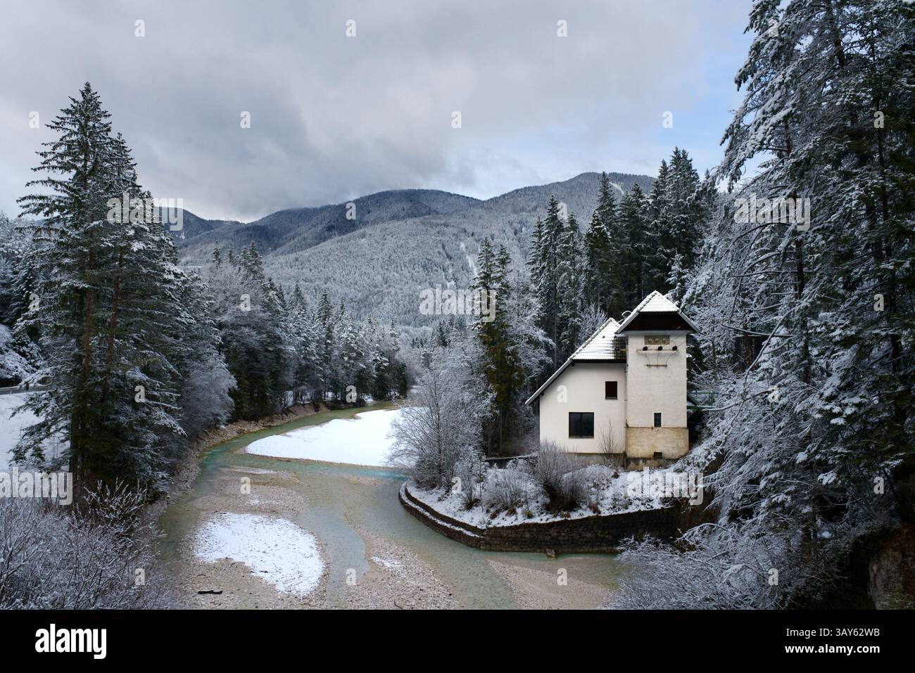 Une maison isolée nichée dans une forêt enneigée surplombe une piscine gelée et une petite cascade. La beauté tranquille de l'hiver enveloppe la scène tranquille. Slovénie Banque D'Images