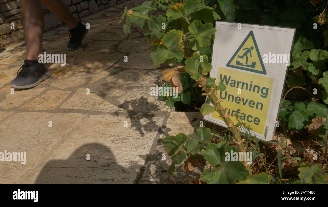 Un piéton passe devant un panneau d'avertissement de surface inégale à Nissaki, Corfou Banque D'Images