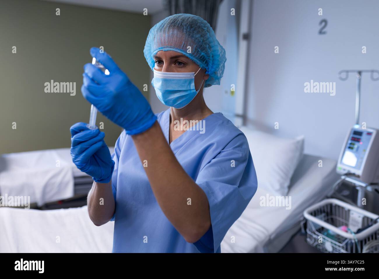 Infirmière femme mi-adulte tirant le flacon de médicament dans la seringue dans la chambre d'hôpital, avec pompe à perfusion Banque D'Images