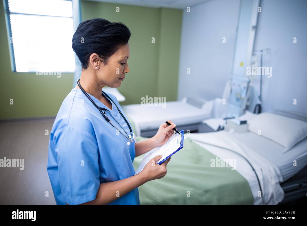 Infirmière mature mettant à jour les dossiers dans la chambre d'hôpital, avec presse-papiers, stylo et stéthoscope, espace de copie Banque D'Images