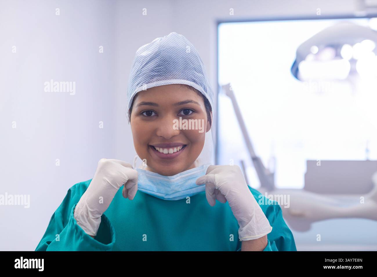 Travailleuse médicale tirant vers le bas le masque facial dans la salle de clinique, portant des gommages verts et des gants Banque D'Images