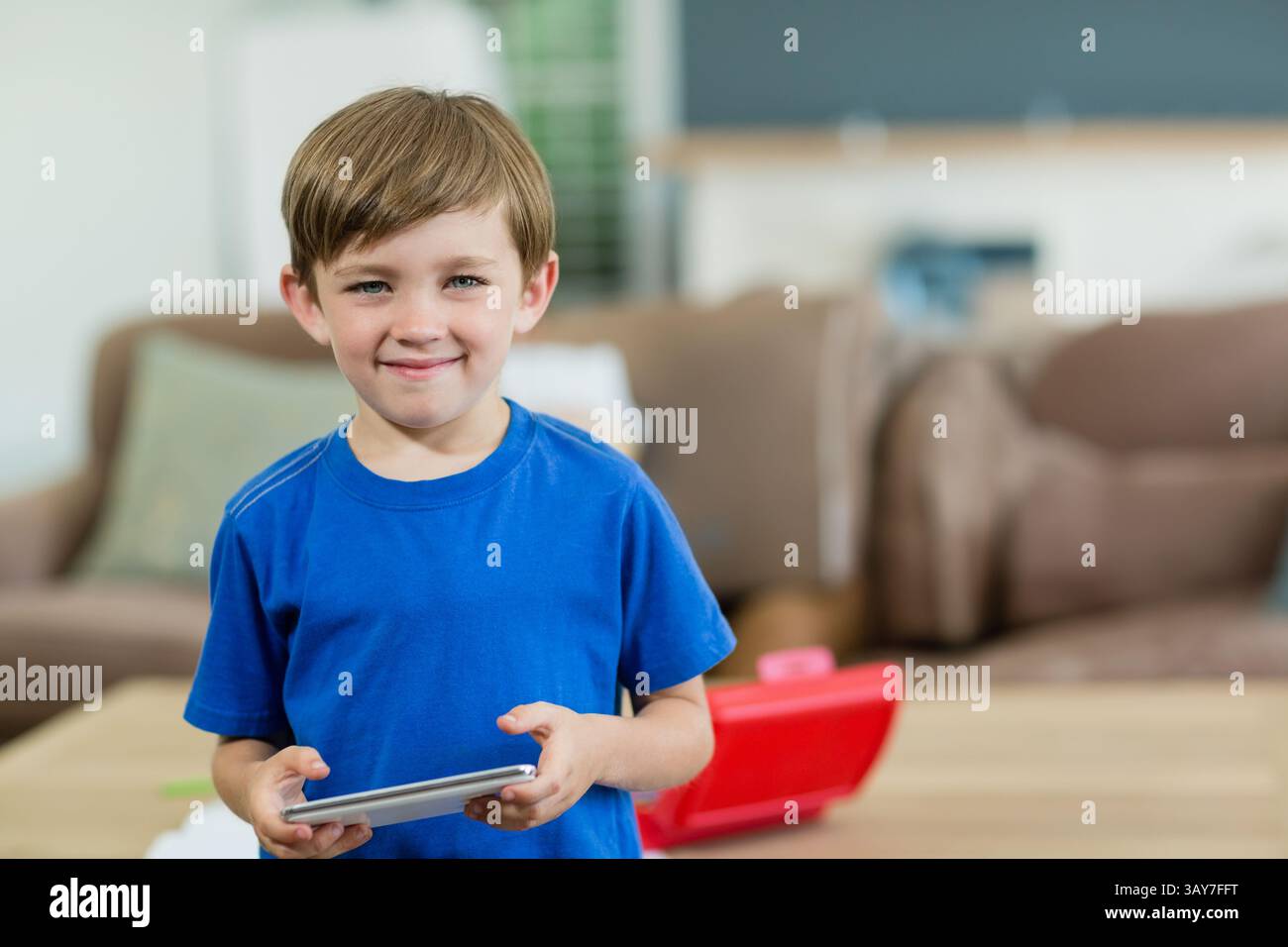 Préscolaire chinoise debout dans le salon, tenant la tablette près du conteneur de jouet rouge et des oreillers de canapé Banque D'Images