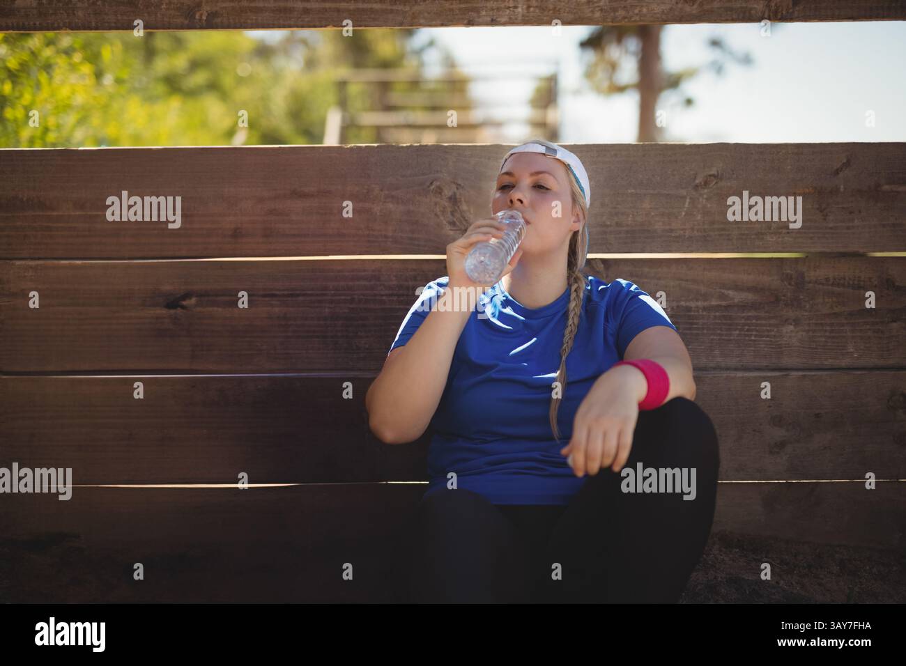 Femme buvant de la bouteille d'eau sur les gradins en bois au terrain de sport, avec bande de sueur, casquette de baseball Banque D'Images