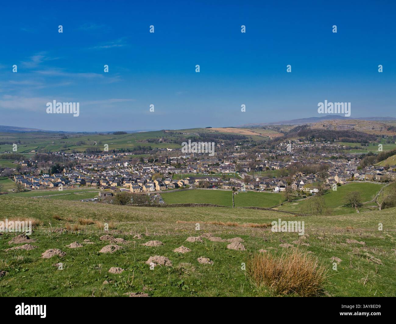 Vue panoramique sur Settle, une ville pittoresque dans les Yorkshire Dales, avec des collines verdoyantes, des maisons dispersées et un ciel bleu clair Banque D'Images