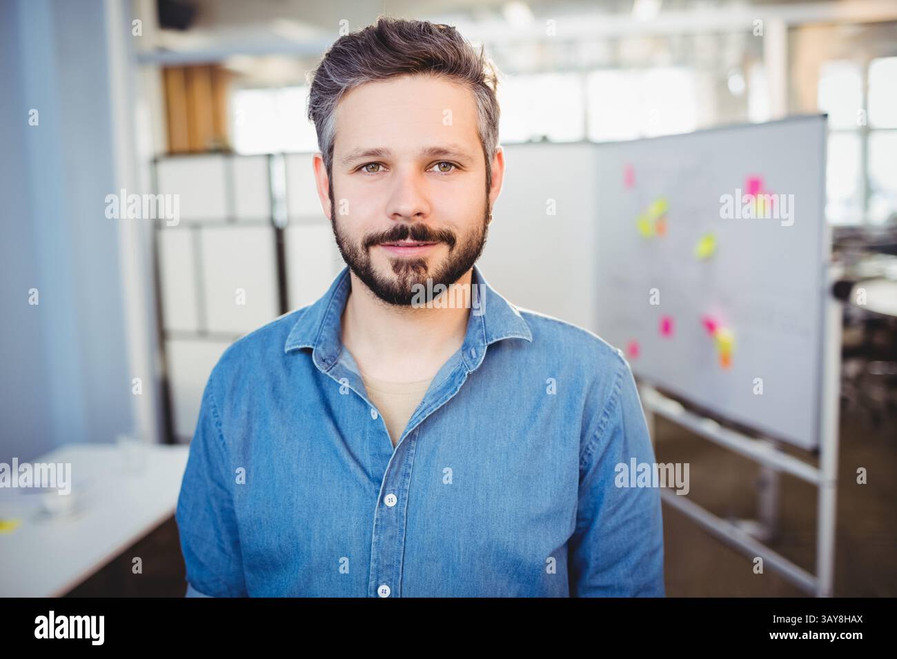 Homme mi-adulte debout dans un bureau ouvert, utilisant un tableau blanc mobile avec des notes autocollantes multicolores Banque D'Images