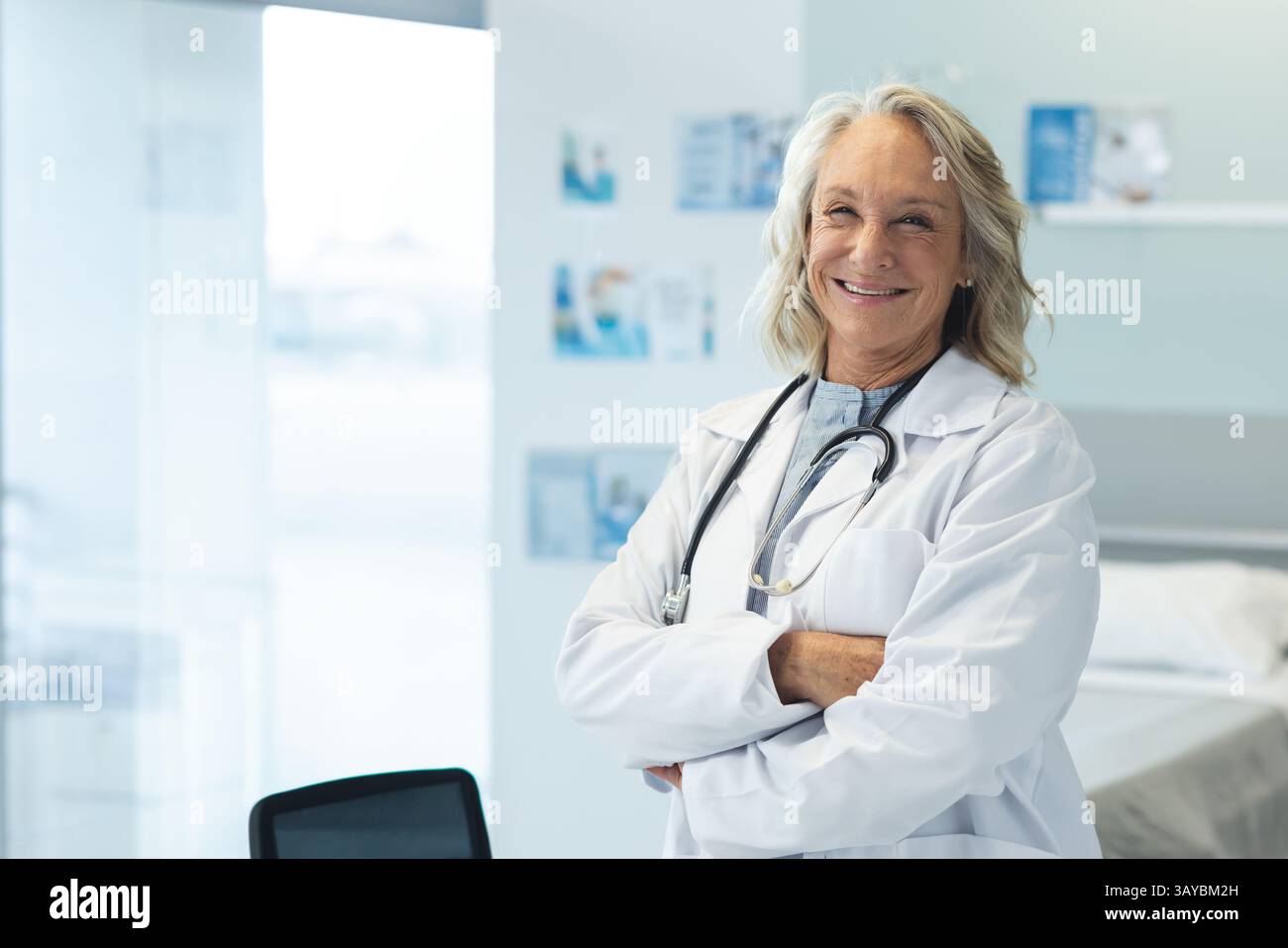 Médecin féminin senior debout dans la salle de clinique moderne avec stéthoscope et lit d'examen, espace de copie Banque D'Images