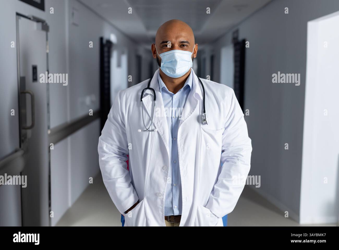 Médecin masculin debout dans le couloir de l'hôpital, avec stéthoscope et masque chirurgical pendant le quart de travail Banque D'Images