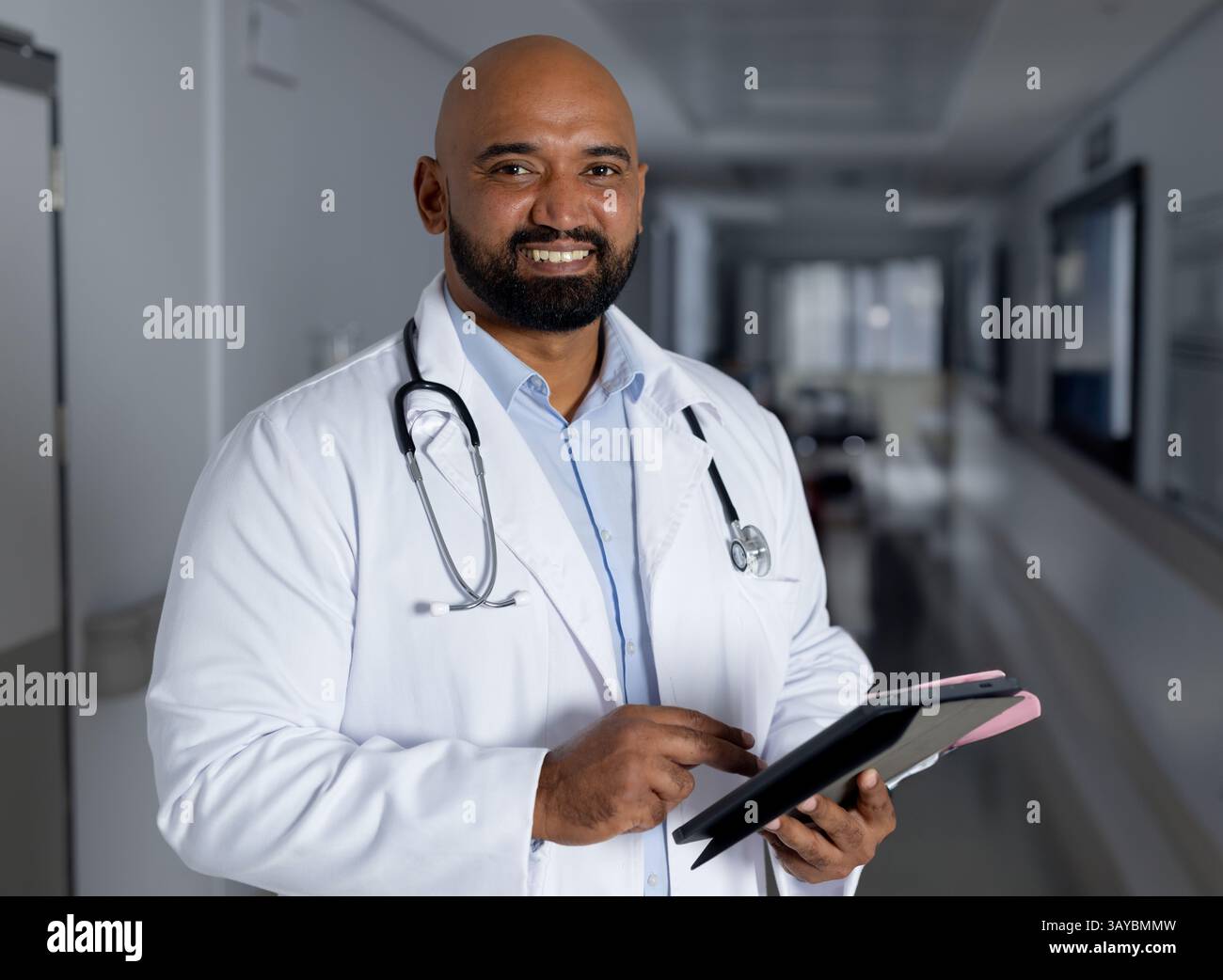 Médecin masculin utilisant la tablette numérique dans le hall de l'hôpital portant blouse de laboratoire et stéthoscope, espace de copie Banque D'Images