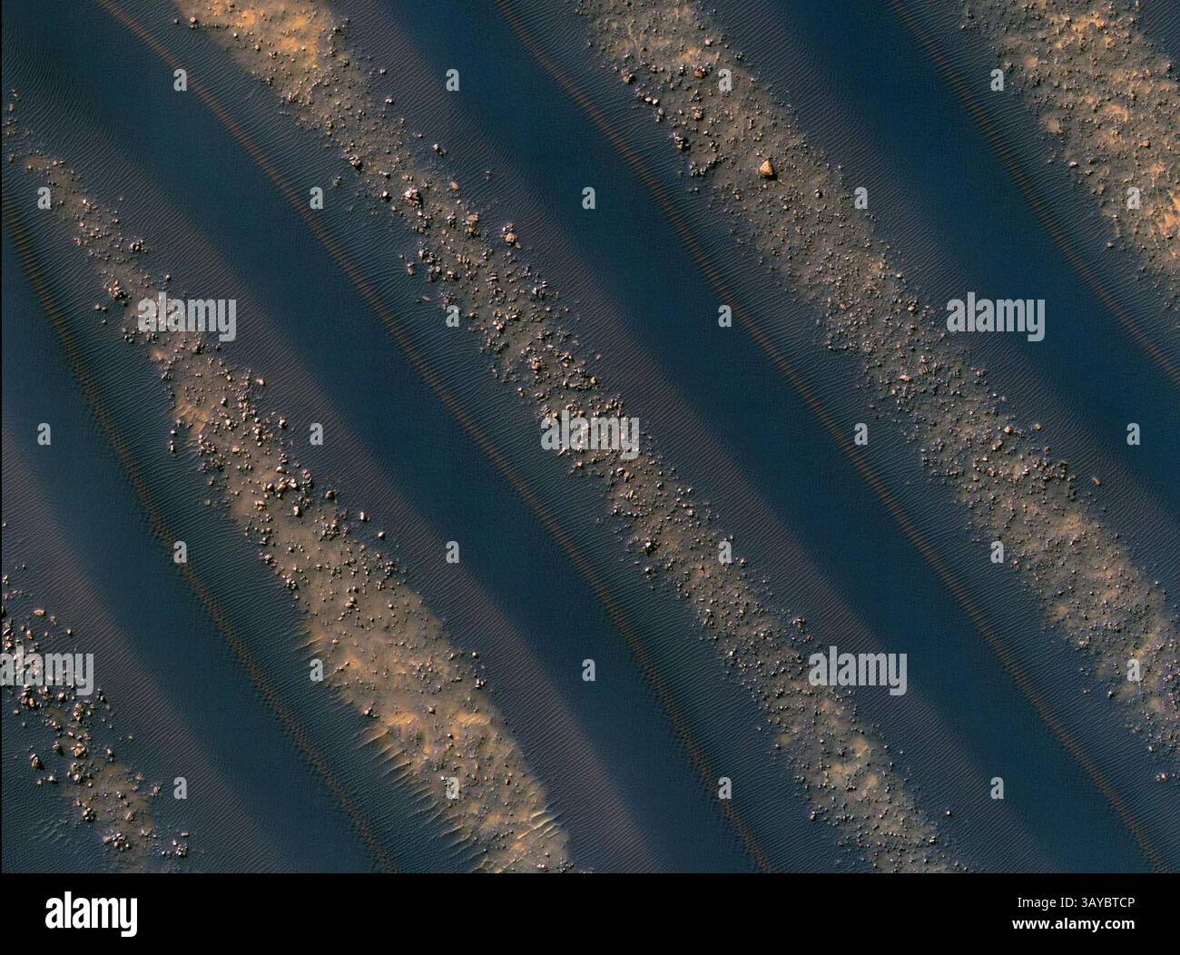 28 décembre 2009 - des dunes de matériaux de la taille du sable ont été piégées sur les planchers de nombreux cratères martiens. Voici un exemple, provenant d’un cratère à Noachis Terra, à l’ouest du bassin d’impact géant de Hellas. La caméra HiRISE (High Resolution Imaging Science Experiment) de mars reconnaissance Orbiter de la NASA a capturé cette vue. Les dunes ici sont linéaires, on pense qu'elles sont dues à des directions de vent changeantes. Par endroits, chaque dune est remarquablement similaire aux dunes adjacentes, y compris une bande rougeâtre (ou de couleur poussière) sur les pentes orientées nord-est. De grands rochers angulaires jonchent le sol entre les dunes. (Crédit image : © JPL-CA Banque D'Images