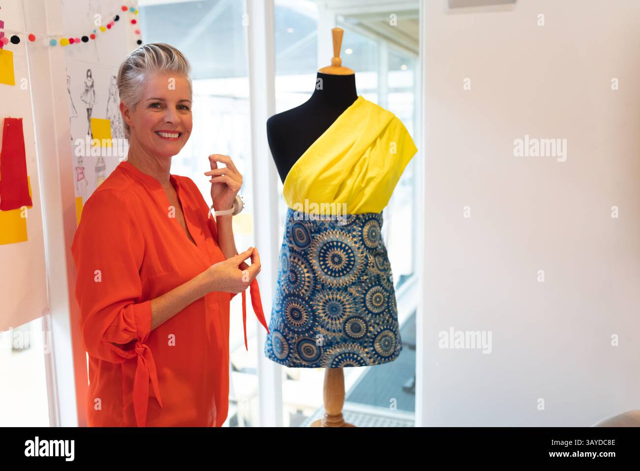 Femme senior tenant le ruban rouge tout en travaillant au studio de design de mode avec forme de robe, espace de copie Banque D'Images