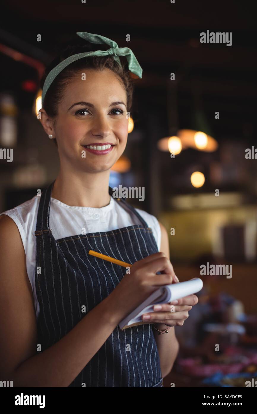 Serveuse souriante et prenant l'ordre dans un restaurant décontracté, avec bloc de commande et crayon jaune Banque D'Images