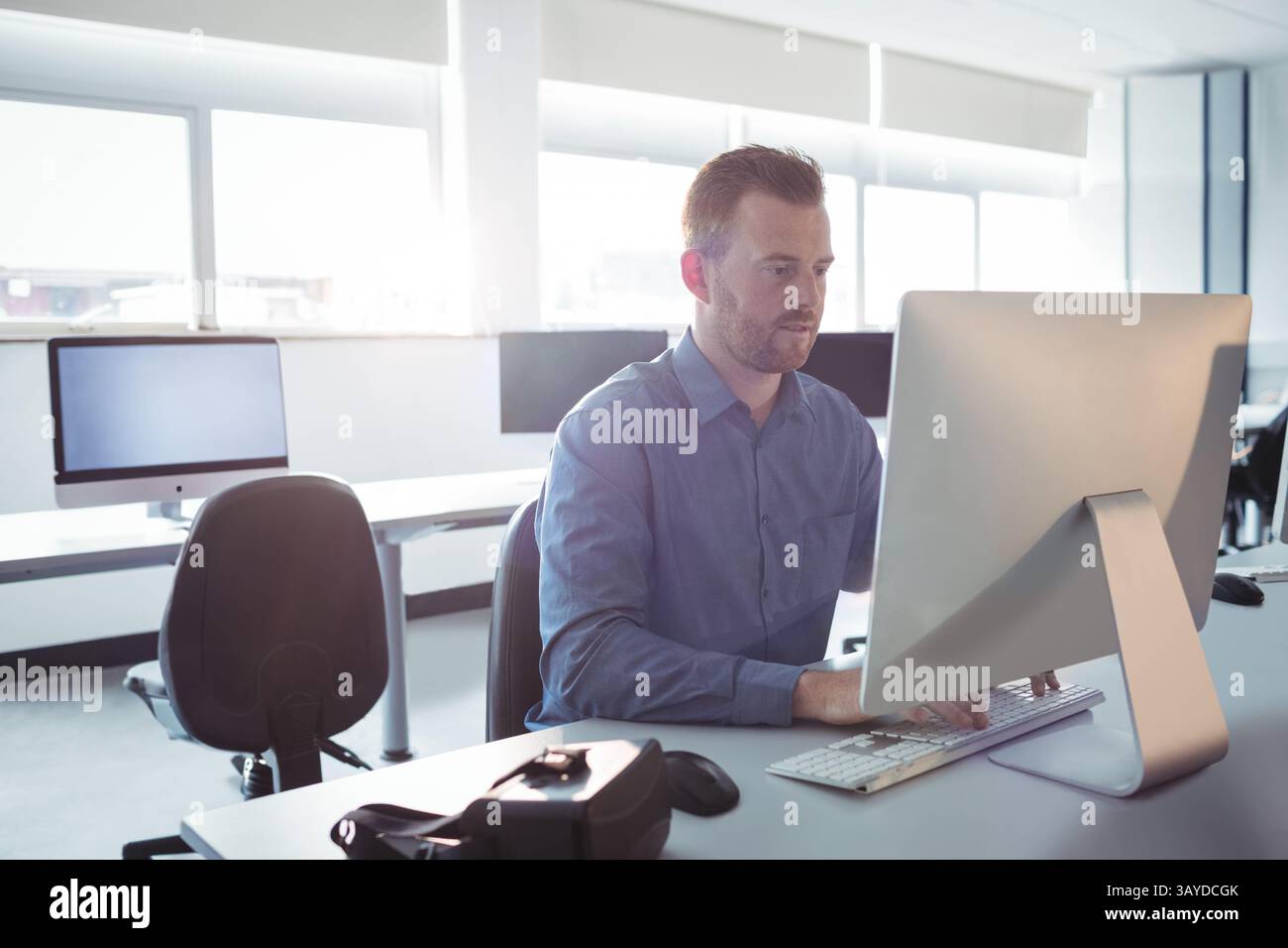 Homme travaillant sur un ordinateur de bureau au bureau ouvert, avec clavier, souris et casque VR Banque D'Images