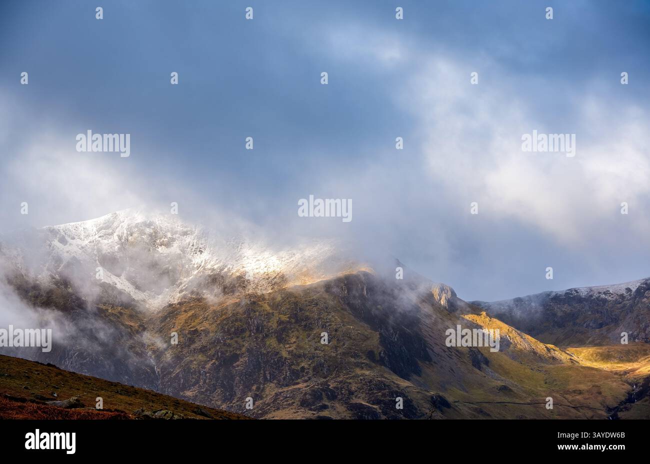 Un tourbillon de brume pèle les sommets enneigés du Glyderau à Cwm Idwal, révélant des poches de soleil changeantes sur les anciennes pentes galloises Banque D'Images