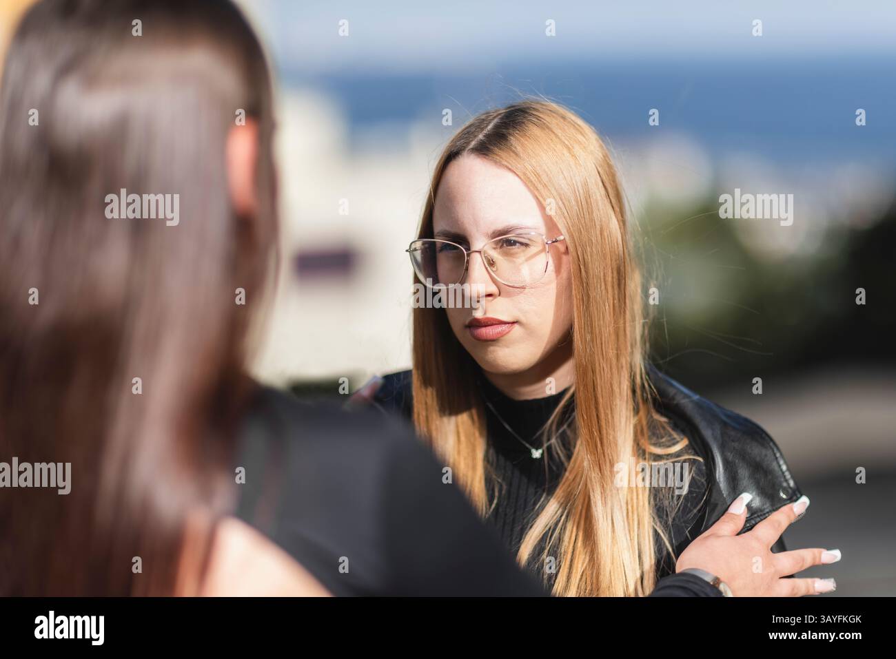 Femme élégante dans des lunettes avec de longs cheveux ayant une conversation sérieuse à l'extérieur Banque D'Images