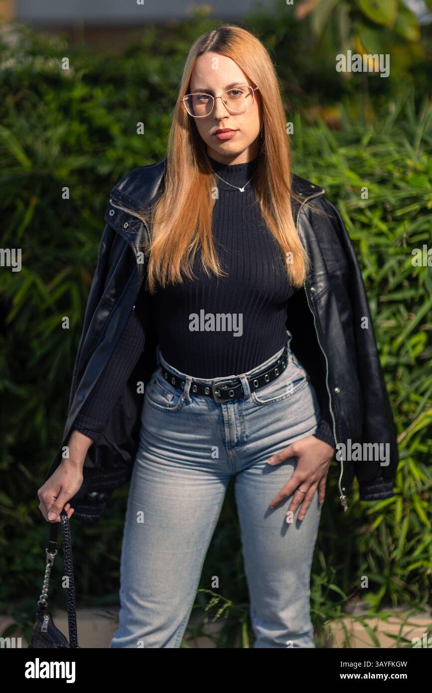 Jeune femme confiante dans le streetwear edgy posant à l'extérieur à la lumière naturelle du soleil Banque D'Images