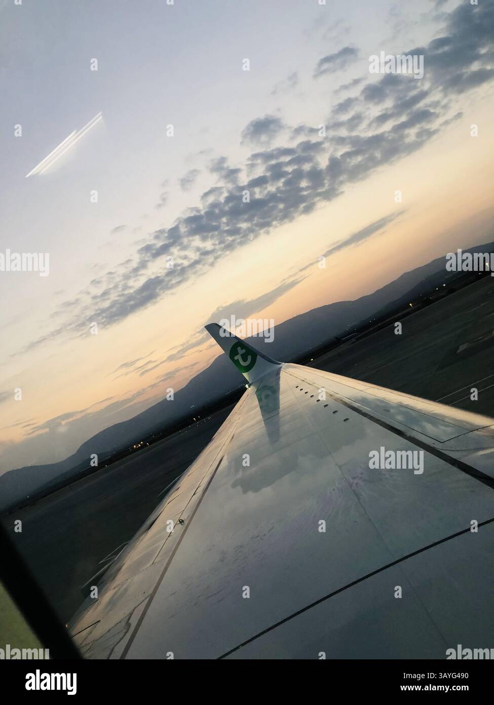 Un coucher de soleil tranquille depuis un avion Transavia à l'aéroport Eleftherios Venizelos d'Athènes, montrant l'aile, le pont à jet avec le logo de la Banque du Pirée, et distan - Image de stock capturée avec un smartphone