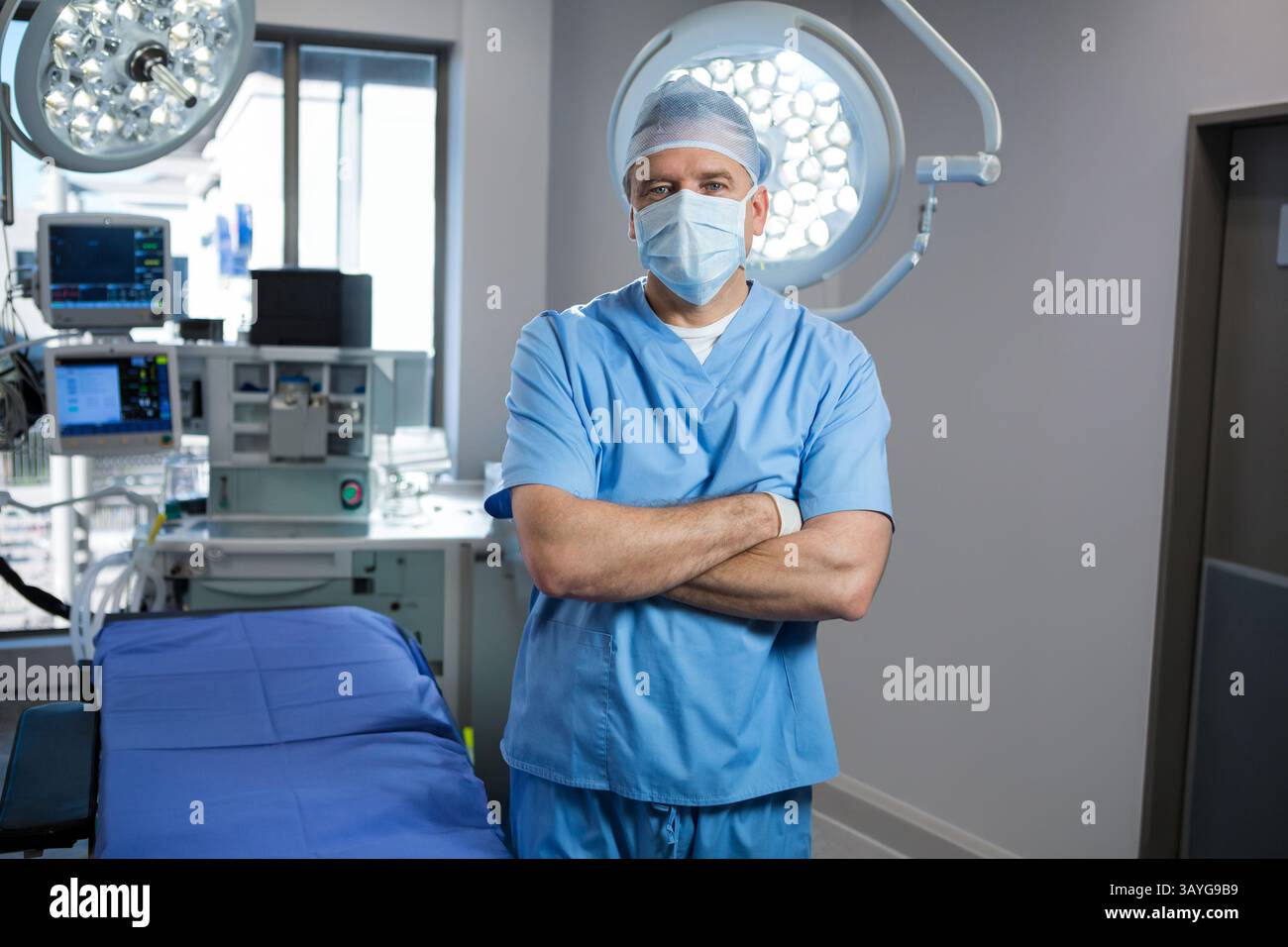 Chirurgien masculin senior debout dans la salle d'opération, avec table, lumières, machine d'anesthésie et moniteurs Banque D'Images