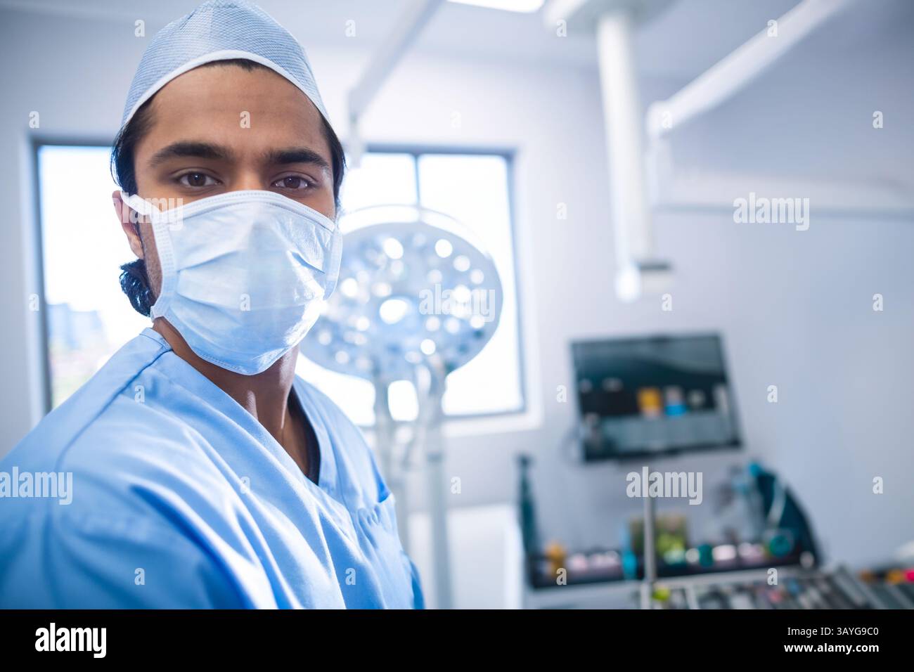Chirurgien masculin asiatique travaillant sous lampe chirurgicale en salle d'opération, vérifiant le moniteur et les plateaux Banque D'Images