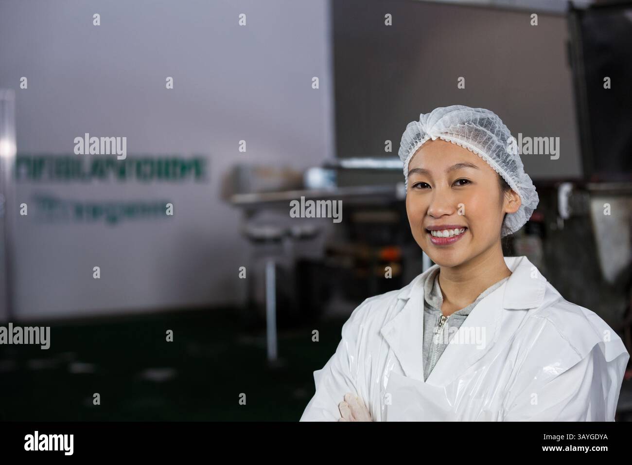 Femme debout, souriant avec les bras croisés dans l'usine de transformation des aliments, blouse de laboratoire, filet à cheveux, espace de copie Banque D'Images