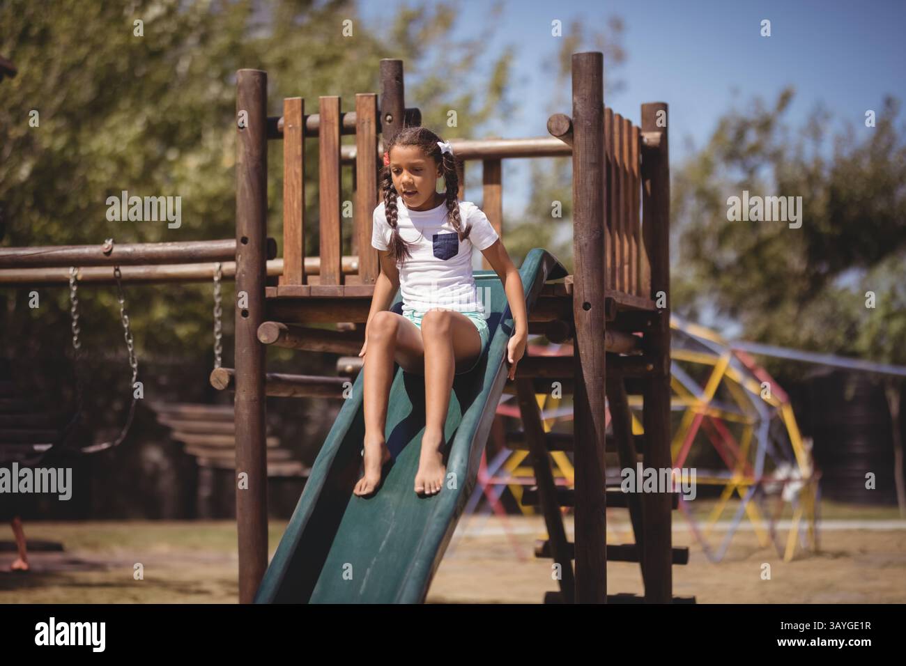 Fille enfant glissant vers le bas de la glissière en plastique vert dans le parc de jeux, profitant du plaisir extérieur ensoleillé Banque D'Images
